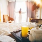 Woman in white robe stay near the window in hotel room. Breakfast in bed.